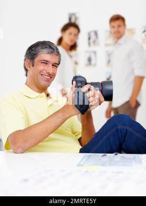 Ein gutaussehender Mann, der sich Bilder in der Kamera ansieht. Porträt eines gutaussehenden Mannes, der Bilder in der Kamera betrachtet und mit Menschen im Hintergrund lächelt. Stockfoto