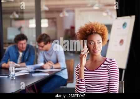 Sie hat sich während eines Meetings bei ihrem Klienten gemeldet. Eine junge Frau, die während eines Meetings in einem Büro mit ihrem Handy spricht. Stockfoto