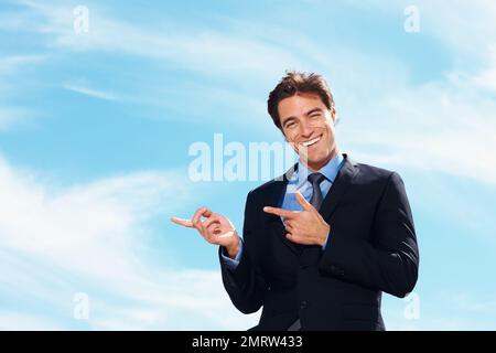 Ein Geschäftsmann zeigt etwas imaginäres gegen den bewölkten Himmel. Ein attraktiver junger Geschäftsmann, der etwas imaginäres gegen den bewölkten Himmel zeigt. Stockfoto