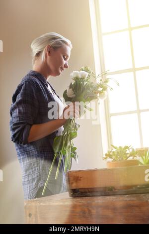 Blumen erhellen die Welt. Eine junge Frau mit einem Blumenstrauß, während sie drinnen am Fenster steht. Stockfoto