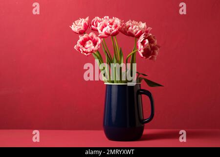 Wunderschöner Frühlingsstrauß aus rosa Tulpen in einer blauen Karaffe auf pinkfarbenem Hintergrund. Color Viva Magenta 18-1750, in 2023 Stockfoto