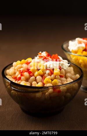 Esquites mit Mais und weißen Kidney Beans, Käse, Mayonnaise und Chili auf dunklem Hintergrund. Mexikanisches Street Food Stockfoto