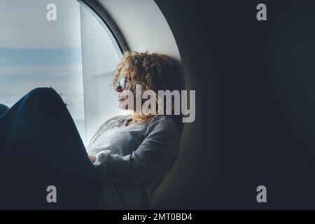 Glückliche Frau, die sich entspannen und reisen kann, sitzt auf einem Bullauge und schaut auf das Wasser draußen. Menschen und Fahrtkonzept Lifestyle. Passagier Stockfoto