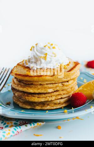 Eine Nahaufnahme eines Stapels gesunder Pfannkuchen, garniert mit Schlagsahne auf einem blauen Teller Stockfoto