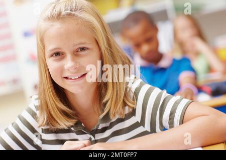 Sie weiß, dass sie eine glänzende Zukunft vor sich hat. Süßes junges Mädchen, das in der Klasse in der Kamera lächelt. Stockfoto