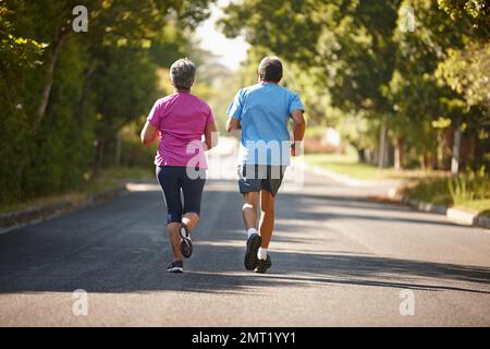 Sich gegenseitig motivieren, gesund zu bleiben. Rückansicht eines erwachsenen Paares, das an einem sonnigen Tag zusammen joggt. Stockfoto