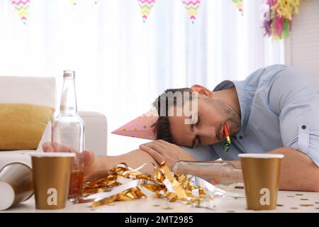 Junger Mann mit festlicher Mütze, der nach der Party am Tisch schläft Stockfoto