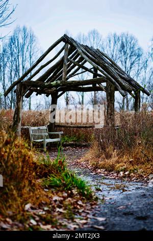 Ein vertikales Bild eines hölzernen Pavillons und eine Bank auf dem trockenen Feld voller herbstgefallener Blätter Stockfoto