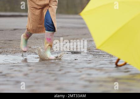Eine Frau in Gummistiefeln, die an regnerischen Tagen über die Pfütze springt Stockfoto