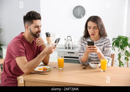 Ein junges Paar mit Smartphones, das zu Hause frühstückt Stockfoto