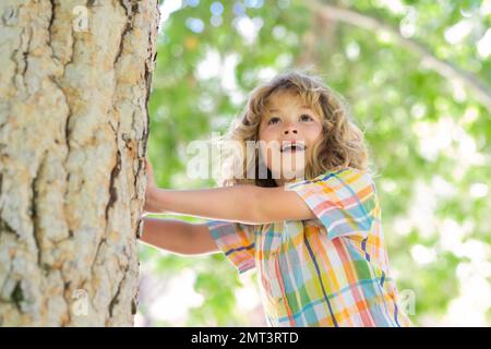 8 Jahre alter Junge, der im Park hoch auf Bäume klettert. Die Höhenangst überwinden. Glückliche Kindheit. Der Junge klettert auf den Baum. Stockfoto