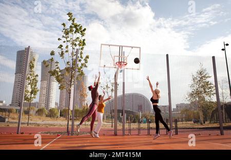 Fröhliche, aktive ältere Frauen spielen Basketball auf dem Stadtplatz. Drei reife Freundinnen verbringen ihre Freizeit im Sport in der Stadt Stockfoto