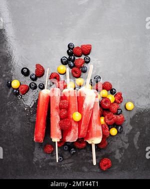 Im Mund schmelzen, meine Güte. Studioaufnahme von Beereneis Lollies, umgeben von einer Auswahl an Beeren. Stockfoto