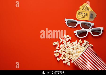 Umgekehrter Pappbecher mit köstlichem Popcorn, Kinokarten und 3D-Brillen auf rotem Hintergrund, flach liegend. Platz für Text Stockfoto