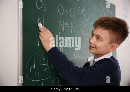 Schuljunge, der chemische Formeln auf Kreidetafeln im Klassenzimmer schreibt Stockfoto