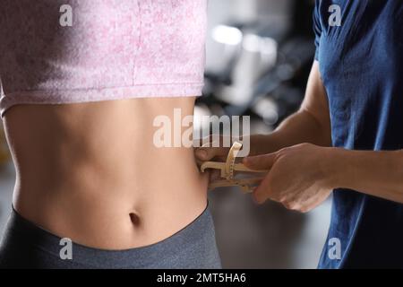 Ernährungswissenschaftlerin misst weibliche Körperfettschicht mit Messschieber drinnen, Nahaufnahme Stockfoto