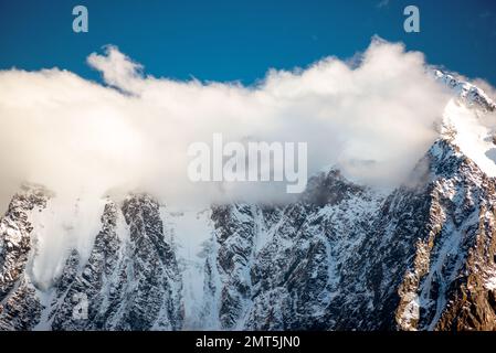 Panoramablick auf die Gipfel der steinernen Berge mit Gletscherzungen und Schnee bedeckt mit weißen Wolken und Nebel in Altai während des Tages. Stockfoto