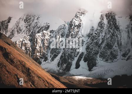 Die Gipfel der steinernen Berge mit Gletscherzungen und Schnee sind in Altai mit weißen Wolken und Nebel bedeckt vor dem Hintergrund eines Felsens. Stockfoto