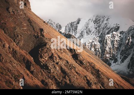 Die Gipfel der steinernen Berge mit Gletscherzungen und Schnee sind in Altai mit weißen Wolken und Nebel bedeckt vor dem Hintergrund eines Felsens. Stockfoto