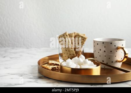 Raffinierte Zuckerwürfel in der Schüssel und aromatischer Tee auf einem weißen Marmortisch. Platz für Text Stockfoto