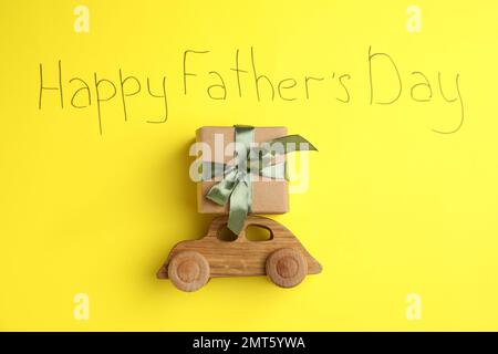 Holzauto, Geschenkbox und Satz HAPPY FATHER's DAY geschrieben auf gelbem Hintergrund, flach liegend Stockfoto