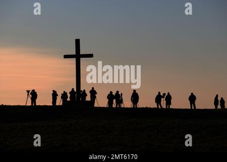 Vogelbeobachter in Silhouette warten auf Eulen neben dem Cross of Peace St. Benets Abbey Norfolk UK GB Sonnenuntergang Januar 2023 Stockfoto
