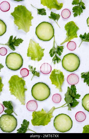 Pflanzlicher Hintergrund aus Salatblättern, Gurkenscheiben, Radieschen und Petersilienblättern auf weißem Hintergrund. Der Begriff der richtigen Ernährung. Der Begriff der richtigen Ernährung. Stockfoto