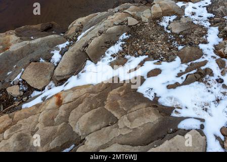 Felsgestein am Ufer mit klarem, schneebedeckten Wasser. Stockfoto