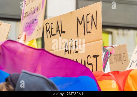 Schwuler junger Erwachsener mit lgbtq-Flagge und Unterstützung eines feministischen Plakats auf einer Demonstration auf der Straße Stockfoto