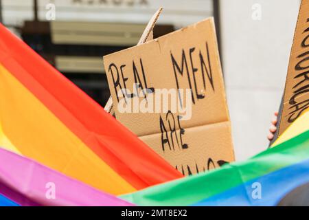 Schwuler junger Erwachsener mit lgbtq-Flagge und Unterstützung eines feministischen Plakats auf einer Demonstration auf der Straße Stockfoto