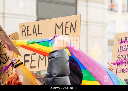 Schwuler junger Erwachsener mit lgbtq-Flagge und Unterstützung eines feministischen Plakats auf einer Demonstration auf der Straße Stockfoto