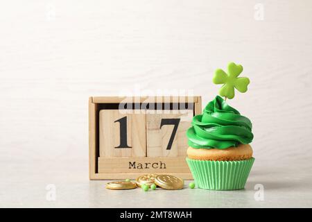 Köstlich dekorierter Cupcake, Holzblock Kalender und Münzen auf einem hellen Tisch. St. Patrick's Day-Feier Stockfoto
