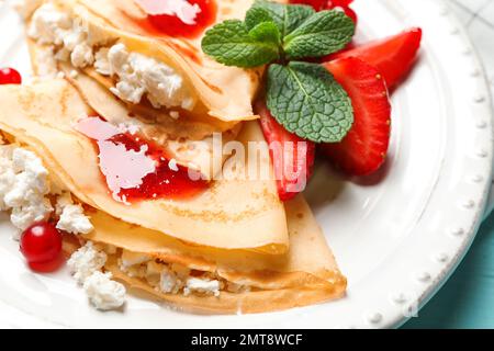 Leckere dünne Pfannkuchen mit Hüttenkäse und Marmelade auf dem Teller, Nahaufnahme Stockfoto