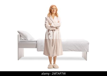 Ganzlängenporträt einer erwachsenen Frau im Bademantel vor einem Bett isoliert auf weißem Hintergrund Stockfoto