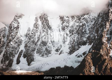 Felsige Berge mit Gletscherzungen und Schnee bedeckt mit weißen Wolken und Nebel in Altai. Stockfoto