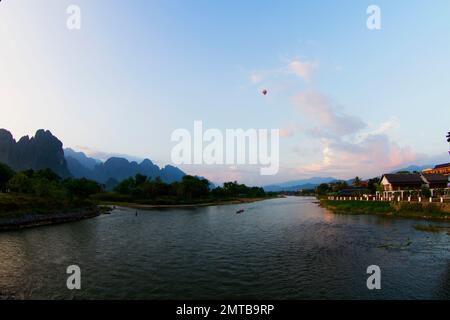 Sie stehen auf der Nam Song Bridge mit Blick auf den Fluss Nam Song mit einem Heißluftballon am Himmel in Vang Vieng, Laos Stockfoto