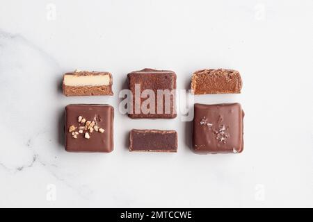 Handgefertigte Schokoladen-Bonbons und geschnittene Stücke Süßigkeiten mit Pralinen und Trüffeln auf weißem Hintergrund mit horizontalem Foto im Kopierraum Stockfoto