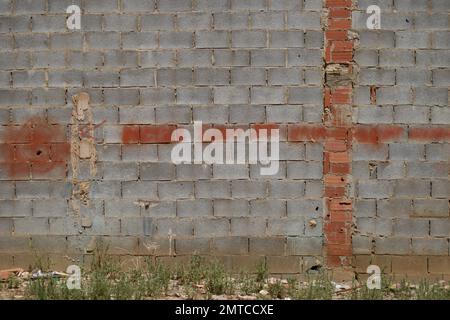 Mauer aus Betonblöcken mit einem Kreuz in rotem Sprühnebel neben einem verlassenen Grundstück, wo Unkraut zwischen den Trümmern und städtischem Müll wächst Stockfoto