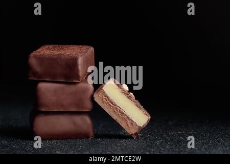 Handgefertigte Schokoladen-Bonbons und geschnittenes Stück Süßigkeiten mit Pralinen und Trüffeln auf schwarzem Hintergrund mit horizontalem Foto im Kopierraum Stockfoto