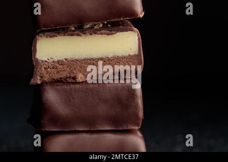 Handgefertigte Schokoladen-Bonbons und geschnittenes Stück Süßigkeiten mit Praline und Trüffel auf schwarzem Hintergrund mit horizontalem Makrofoto Stockfoto