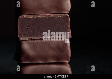 Handgefertigte Schokoladen-Bonbons und ein Stückchen Süßigkeiten mit Trüffel auf schwarzem Hintergrund mit horizontalem Makrofoto Stockfoto