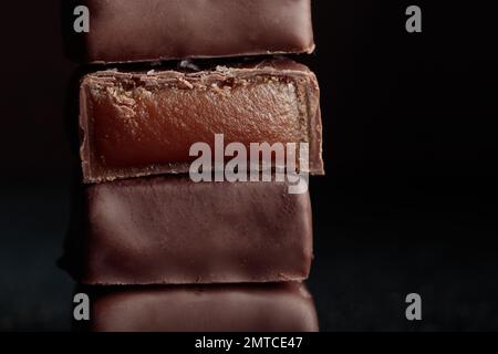 Schokolade, handgefertigte Bonbons und geschnittenes Stück Bonbon mit Karamell auf schwarzem Hintergrund mit horizontalem Makrofoto Stockfoto