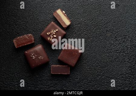 Handgefertigte Schokoladen-Bonbons und geschnittene Stücke Süßigkeiten mit Pralinen und Trüffeln auf schwarzem Hintergrund mit horizontalem Banner Stockfoto