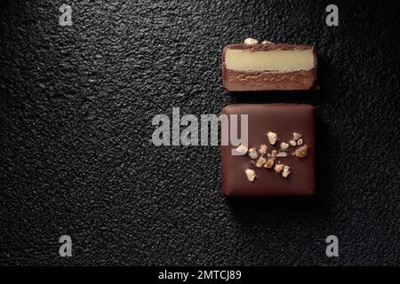 Handgefertigte Schokoladen-Bonbons und geschnittenes Stück Süßigkeiten mit Pralinen und Trüffeln auf schwarzem Hintergrund mit horizontalem Foto im Kopierraum Stockfoto