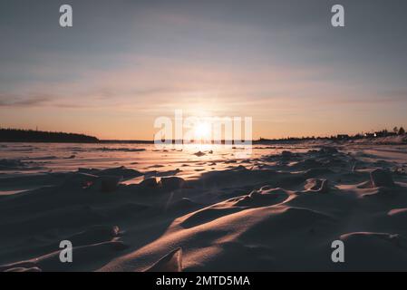 Die helle Wintersonne untergeht über dem Wald am Horizont und wirft Rochen auf die hervorstehenden Eisschollen auf dem Vilyui River in Yakutia. Stockfoto