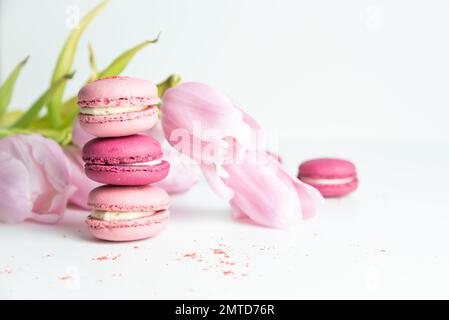 Stapel rosafarbener Makronen mit rosafarbenen Tulpen auf weißem Hintergrund Stockfoto