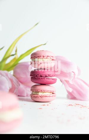 Stapel rosafarbener Makronen mit rosafarbenen Tulpen auf weißem Hintergrund Stockfoto