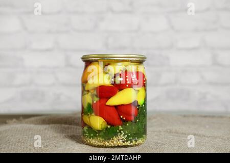 Mini-Chili-Paprika in Rot-, Gelb- und Orangenfarben, in Glasdosen mit Kräutern auf einem Holztisch. Hausgemachte eingelegte Paprika im asiatischen Stil. Vorb Stockfoto