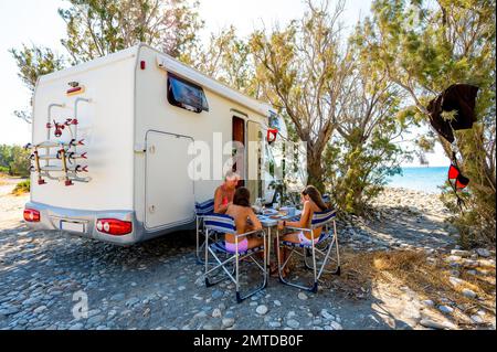 Familien, die mit dem Wohnmobil unterwegs sind, frühstücken am Strand. Reisende auf einem aktiven Familienurlaub mit Wohnmobil RV am Strand unter einem geparkt Stockfoto
