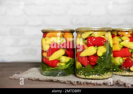 Mini-Chili-Paprika in Rot-, Gelb- und Orangenfarben, in Glasdosen mit Kräutern auf einem Holztisch. Hausgemachte eingelegte Paprika im asiatischen Stil. Vorb Stockfoto